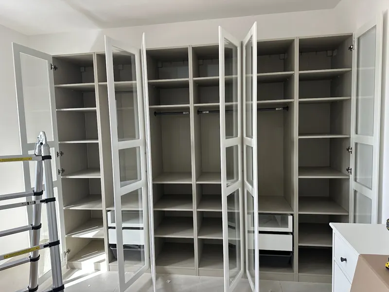 ארון בגדים גדול עם דלתות זכוכית פתוחות ומדפים ריקים, לצד סולם